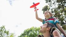 Low angle view of a boy with toy aeroplane sitting on father27s shoulders at the park