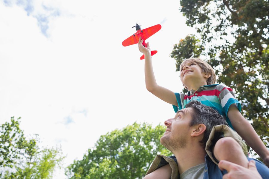 Low angle view of a boy with toy aeroplane sitting on father27s shoulders at the park