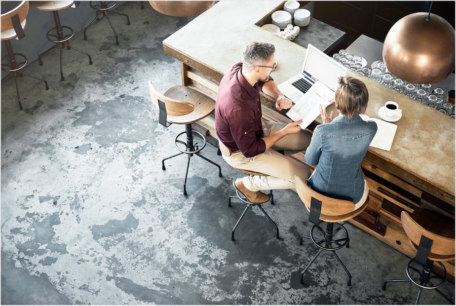 Two people sitting at a desk looking at a laptop and important documents.