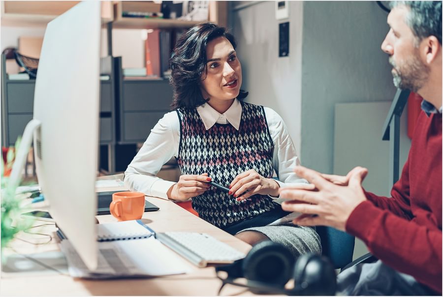 A woman and a man having a discussion in front of a computer in an office.