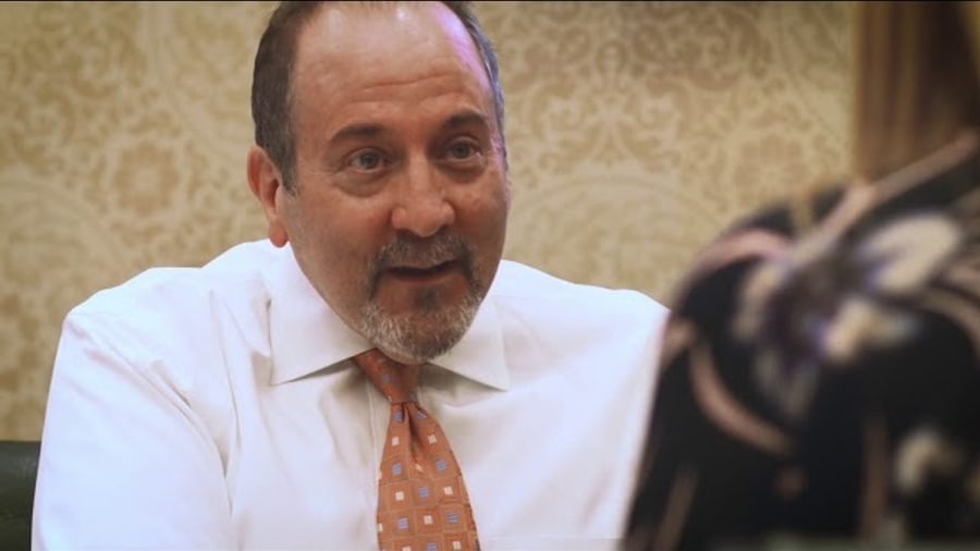 A man in a shirt and tie, speaking to clients at his desk.