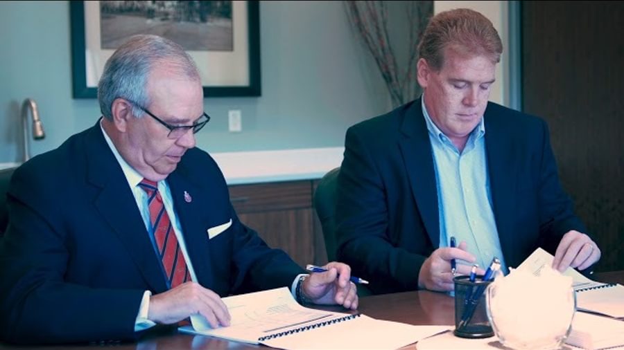 Two men in business attire at a desk. They are both looking at reports.
